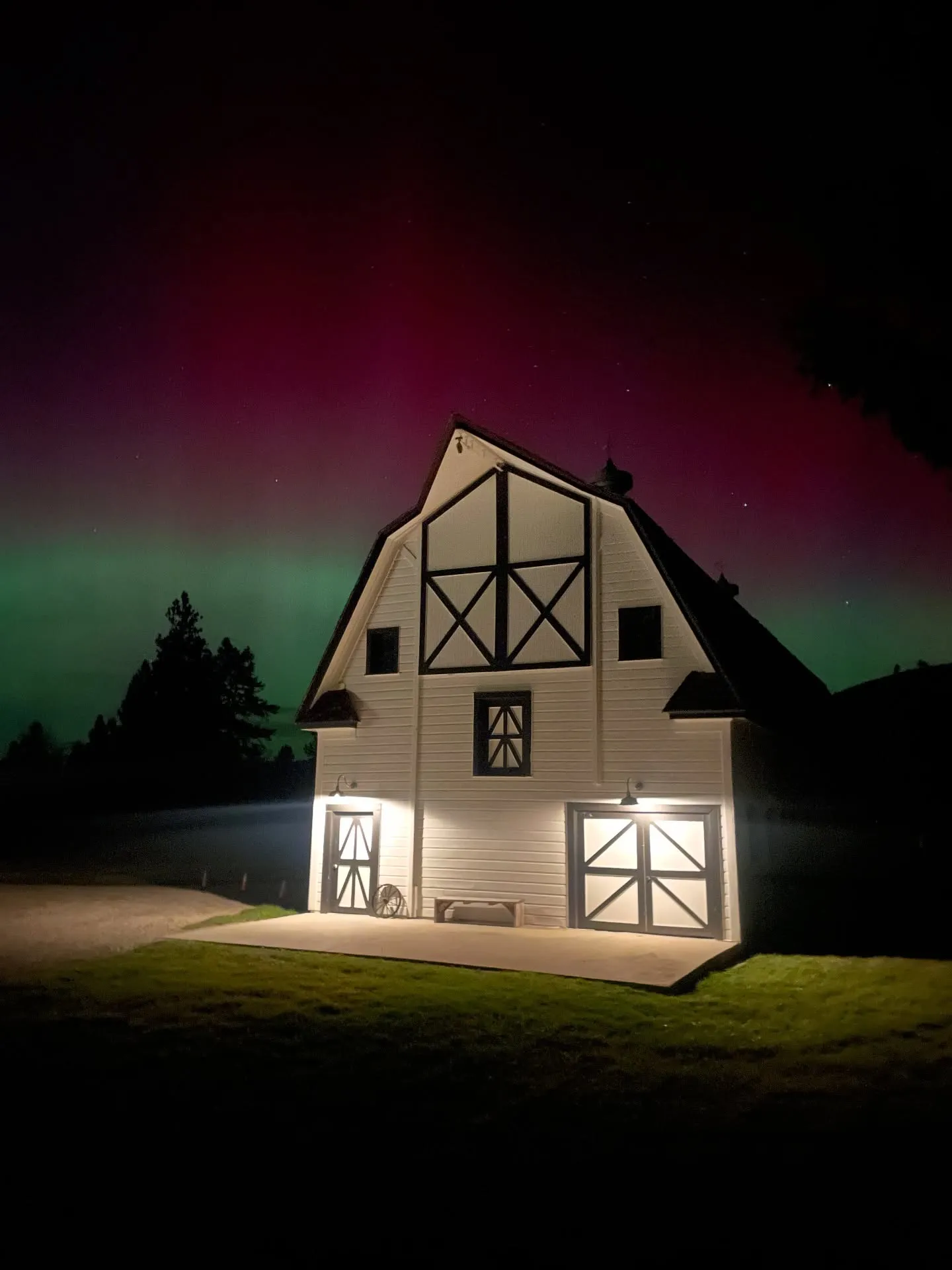 The ranch barn lit from within at night under the northern lights