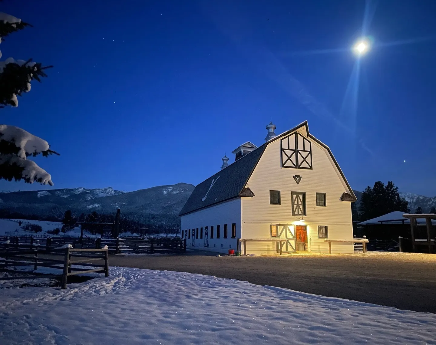 The white barn glowing under a full moon on a snowy night, mountains behind